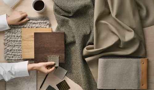 Person selecting fabric swatches on a table with various textures and colors.