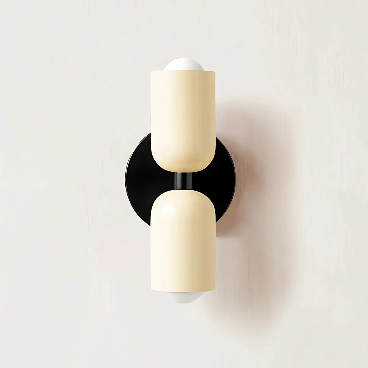 Modern wall sconce with two cylindrical beige shades and a black base on a light gray background