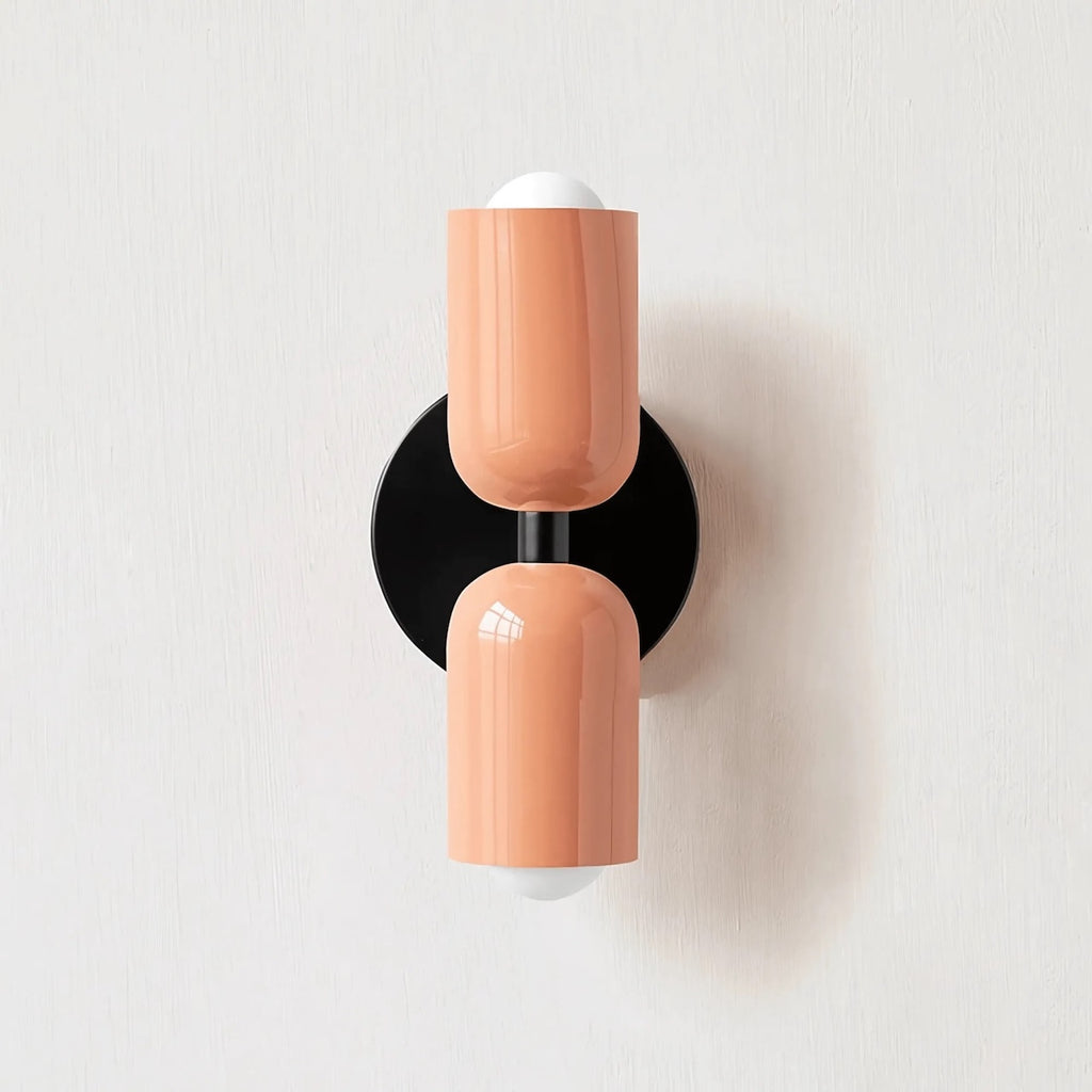 Wall-mounted lamp with two peach-colored cylindrical shades on a white background