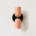 Wall-mounted lamp with two peach-colored cylindrical shades on a white background